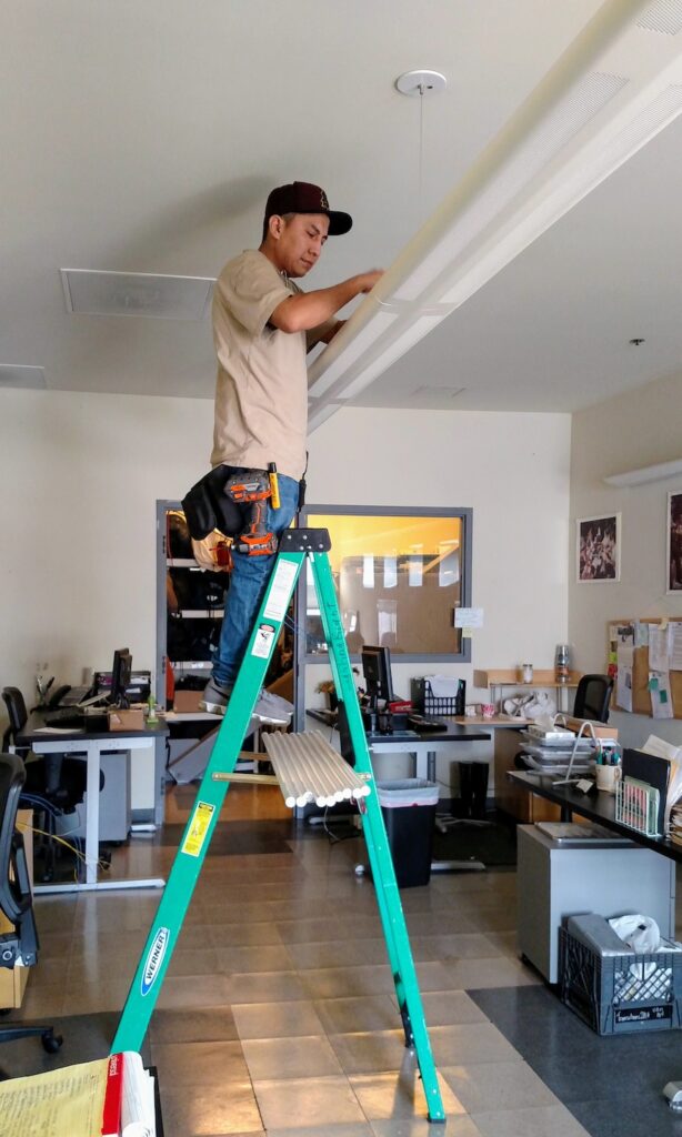 Contractor on a latter installing LED lights at an office of the women's building