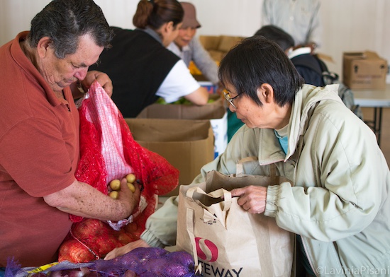 wo individuals receiving food at a pantry, packing potatoes and onions into bags. The image highlights the food pantry's role in supporting individuals and families in need within the community.