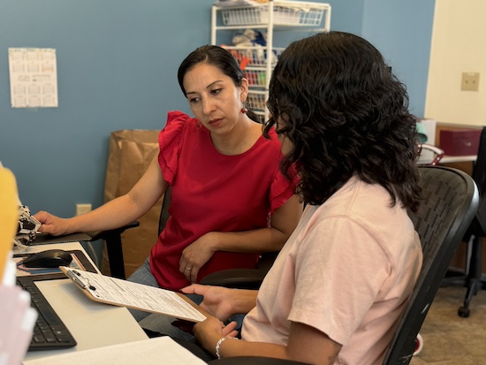 A staff member attentively helps a community member with paperwork at a desk, showcasing The Women's Building dedication to one-on-one support and resources for those in need.